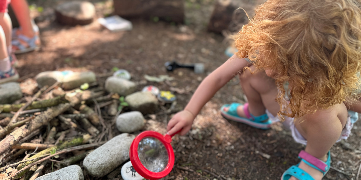 Girl holding magnifying glass to ricks with drawing on them